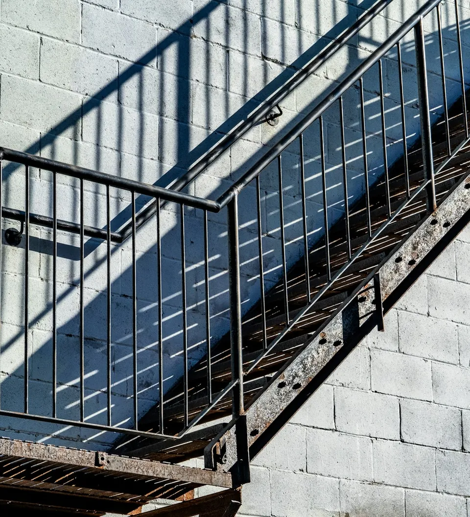 Escalera metálica exterior con baranda junto a un muro