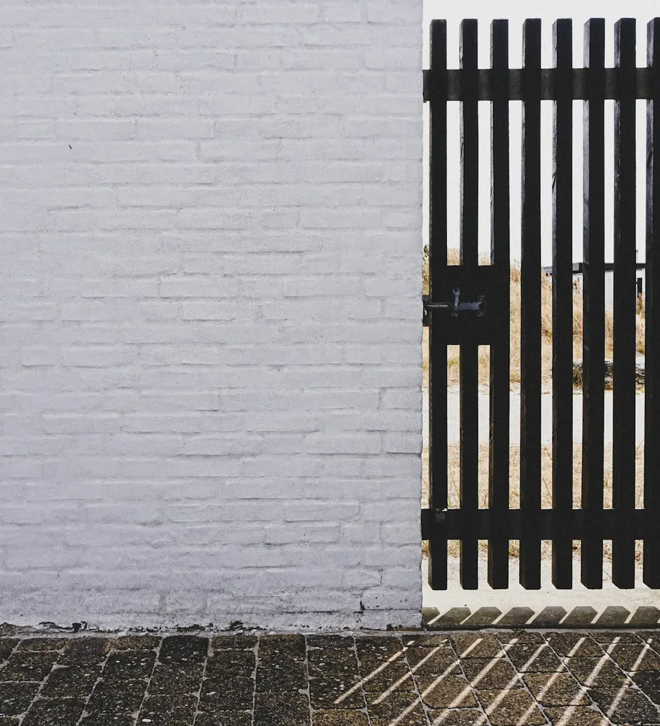 Puerta de reja negra de barrotes junto a un muro blanco